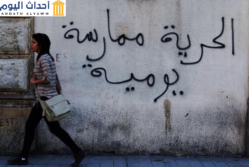 امرأة تونسية تسير أمام جدار كُتِبت عليه عبارة "الحرية ممارسة يومية" في العاصمة تونس