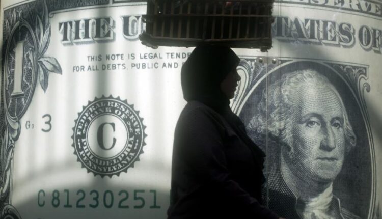 بائعة مصرية تمر بجوار ملصق للدولار الأمريكي خارج مكتب للصيرفة في القاهرة، مصر