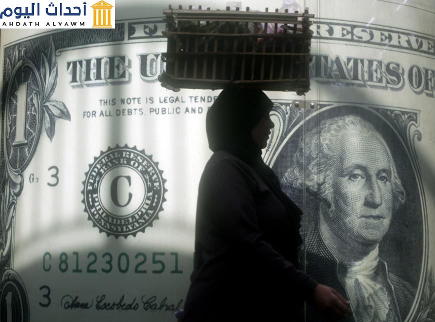 بائعة مصرية تمر بجوار ملصق للدولار الأمريكي خارج مكتب للصيرفة في القاهرة، مصر