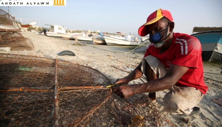 صياد يرتدي قناعا للوجه ويجهز أدوات عمله على ساحل المنامة
