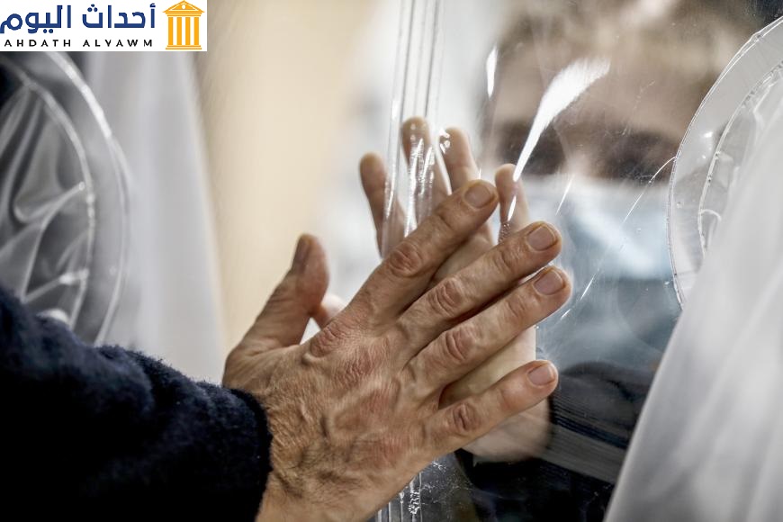 Relatives touch each other's hand through a plastic film screen and a glass to avoid contracting Covid-19 at the San Raffaele center in Rome, Italy