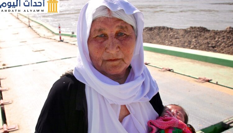 سيدة أيزيدية كبيرة في السن تحمل طفلا تفر من سنجار وتعاود الدخول للعراق عبر سوريا