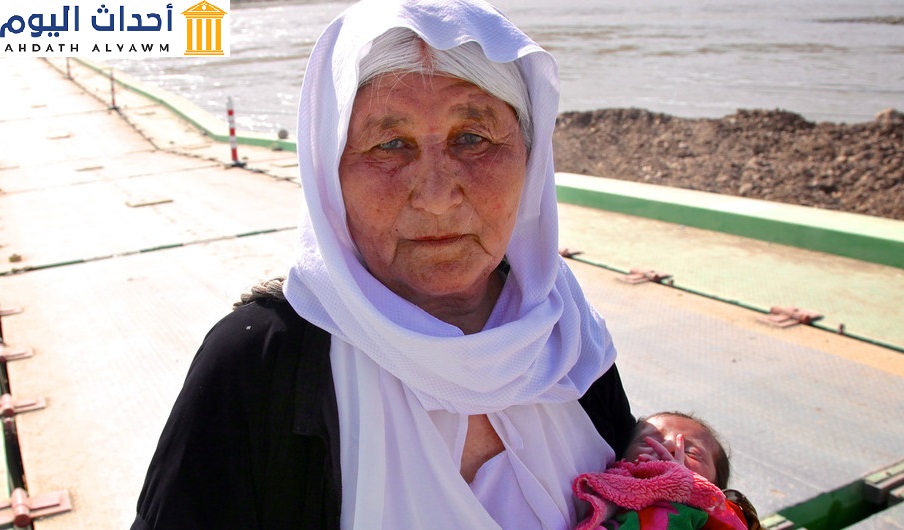 سيدة أيزيدية كبيرة في السن تحمل طفلا تفر من سنجار وتعاود الدخول للعراق عبر سوريا
