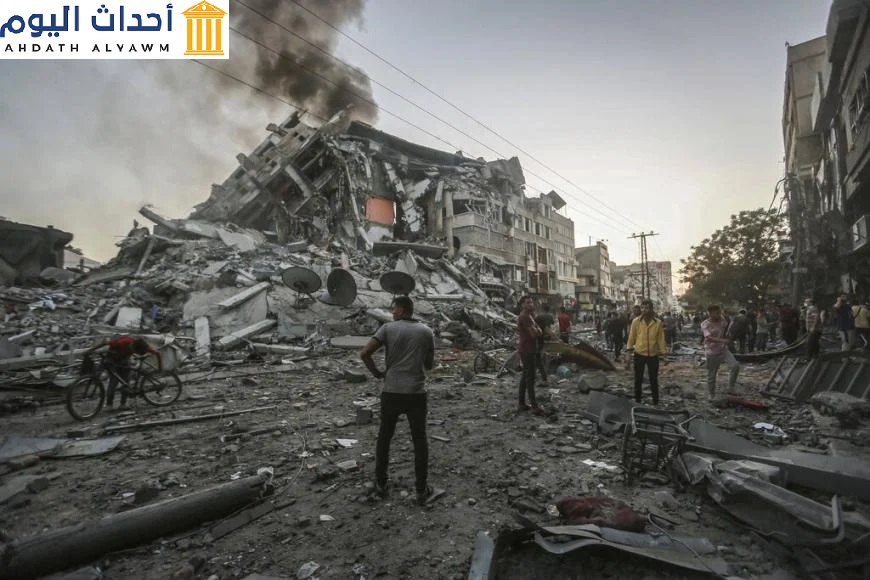 أشخاص في قطاع غزة يقفون إلى جانب موقع برج الشروق المنهار جراء غارة إسرائيلية في 12 مايو/أيار