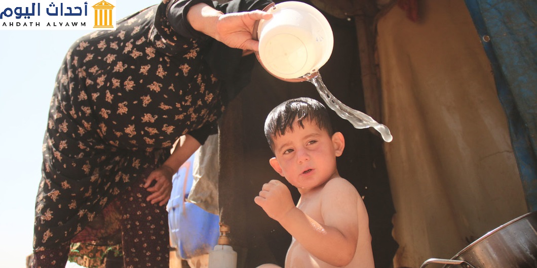جدة تقوم بتغسيل حفيدها في أحد مخيمات النازحين بريف إدلب