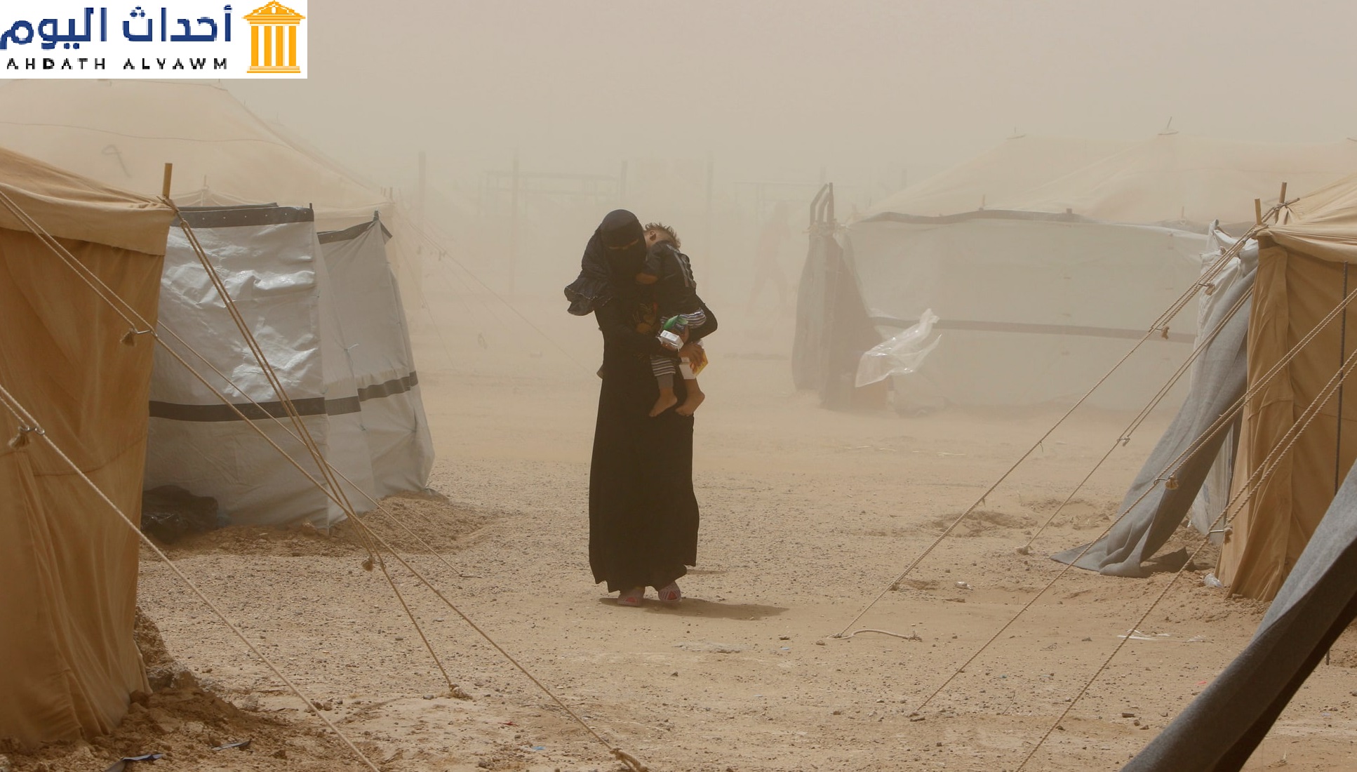 أم تحمل طفلها خلال عاصفة رملية في مخيم للاجئين في مدينة عامرية الفلوجة بالعراق