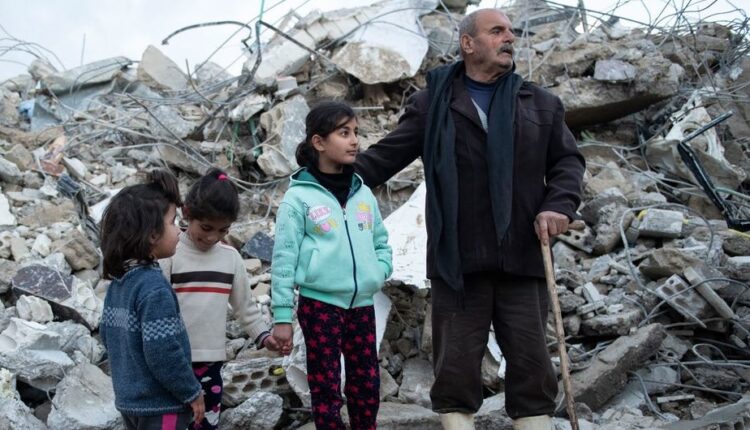 عائلة من منطقة الرميلة في قضاء جبلة شمال غرب سوريا تقف بالقرب من منزلها المدمر