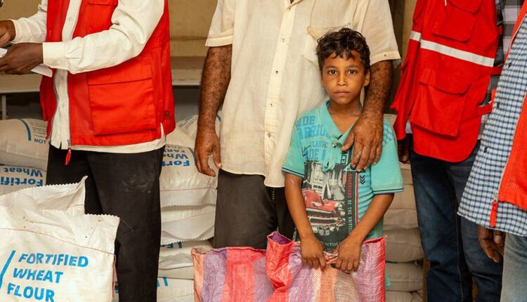 طفل نازح ينتظر مع والده توزيع المواد الغذائية في بورتسودان